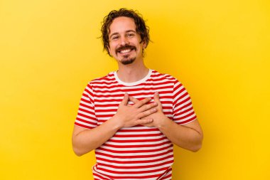 Sarı arka planda izole olmuş genç beyaz adam gülüyor, elini yüreğine koyuyor, mutluluk kavramını koruyor..