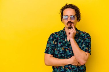 Sarı arka planda izole edilmiş yaz kıyafetleri giyen genç beyaz adam şüpheli ve şüpheci bir ifadeyle yana bakıyor..