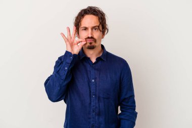 Beyaz arka planda izole edilmiş beyaz tenli genç bir adam parmakları dudaklarında bir sır saklıyor..