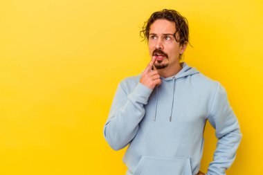 Sarı arka planda izole edilmiş genç beyaz adam şüpheli ve şüpheci bir ifadeyle yana bakıyor..