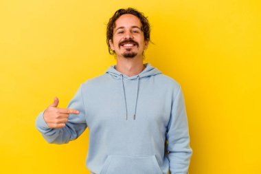 Sarı arka planda izole edilmiş genç beyaz bir adam gömlek fotokopi alanını elle gösteriyor, gururlu ve kendinden emin.