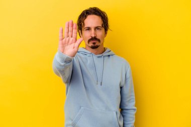 Sarı arka planda izole edilmiş genç beyaz adam elini uzatmış, dur işareti göstererek seni engelliyor..