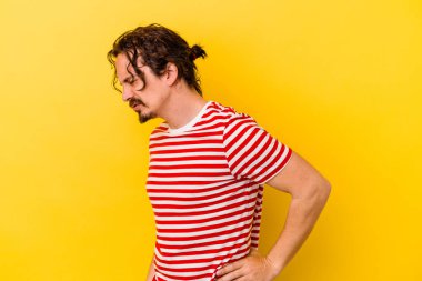 Sarı arka planda izole edilmiş beyaz bir adam sırt ağrısı çekiyor..