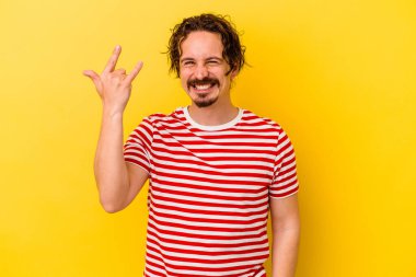 Sarı arka planda izole edilmiş genç beyaz adam parmaklarıyla kaya hareketi gösteriyor.