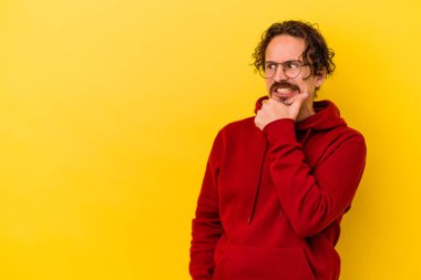 Kafkasyalı genç adam sarı arka planda izole edilmiş kafasının arkasına dokunuyor, düşünüyor ve bir seçim yapıyor..