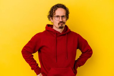 Sarı arka planda izole edilmiş genç beyaz adam hoşnutsuzca kaşlarını çatmış, kollarını kavuşturmuş..