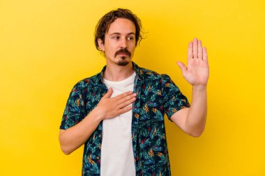 Sarı arka planda izole edilmiş genç beyaz adam yemin ediyor, elini göğsüne koyuyor..