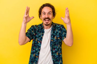 Sarı arka planda izole genç beyaz adam hoş bir sürpriz alıyor, heyecanlı ve el kaldırıyor..
