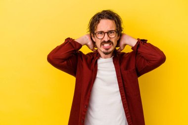 Kafkasyalı genç adam sarı arka planda izole edilmiş kafasının arkasına dokunuyor, düşünüyor ve bir seçim yapıyor..