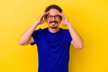 Sarı arka planda izole genç beyaz adam hoş bir sürpriz alıyor, heyecanlı ve el kaldırıyor..