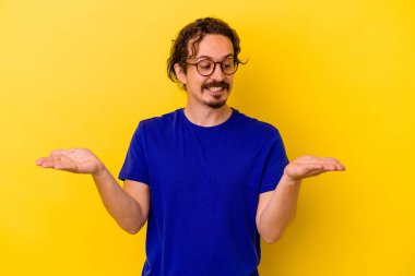 Sarı arka planda izole edilmiş genç beyaz bir adam elinde avuç içi bir şeyle kameraya sunuyor..