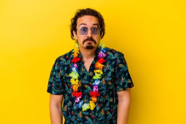 Sarı arka planda izole edilmiş Hawaii kolyesi takan genç beyaz adam omuzlarını silker ve gözleri açık kalır..