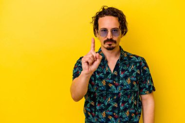 Sarı arka planda izole edilmiş yaz kıyafetleri giyen genç beyaz adam bir numarayı parmağıyla gösteriyor..