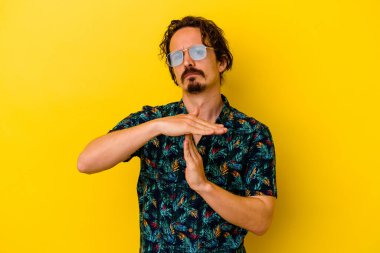 Sarı arka planda izole edilmiş yaz kıyafetleri giyen genç beyaz bir adam bir mola hareketi gösteriyor..