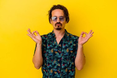 Sarı arka planda izole edilmiş yaz kıyafetleri giyen genç beyaz adam sıkı çalışma gününden sonra dinleniyor. Yoga yapıyor..