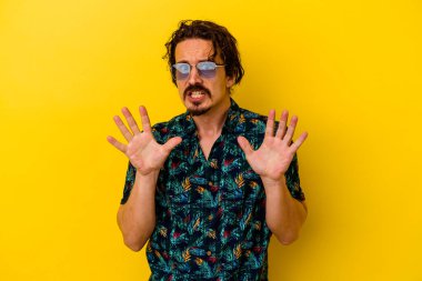 Sarı arka planda izole edilmiş yaz kıyafetleri giyen genç beyaz bir adam tiksinti belirtisi gösteren birini reddediyor..