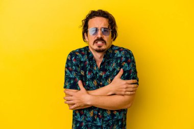 Sarı arka planda izole edilmiş yaz kıyafetleri giyen genç beyaz adam düşük ateş ya da hastalık nedeniyle soğuyor..