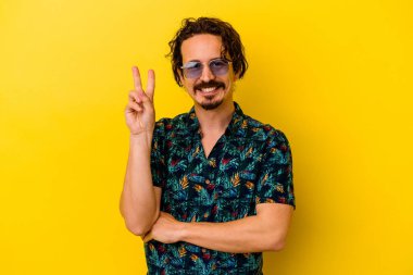 Sarı arka planda izole edilmiş yaz kıyafetleri giyen genç beyaz adam iki numarayı parmaklarıyla gösteriyor..