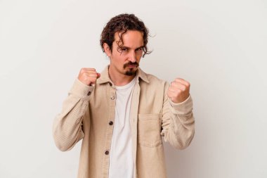 Beyaz arka planda izole edilmiş genç beyaz bir adam yumruğunu kameraya gösteriyor, agresif bir yüz ifadesi..