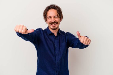 Beyaz arka planda izole edilmiş genç beyaz bir adam iki parmağını da kaldırıyor, gülümsüyor ve kendinden emin..