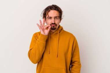 Beyaz arka planda izole edilmiş beyaz tenli genç bir adam parmakları dudaklarında bir sır saklıyor..