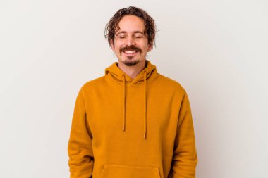 Beyaz arka planda izole edilmiş genç beyaz adam gülüyor ve gözlerini kapıyor, rahatlamış ve mutlu hissediyor..