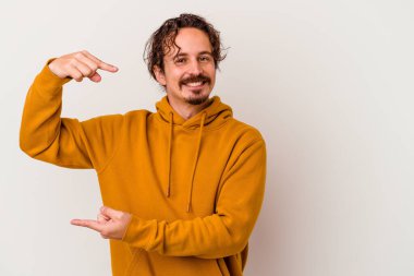 Beyaz arka planda izole edilmiş genç beyaz bir adam işaret parmaklarıyla küçük bir şey tutuyor, gülümsüyor ve kendinden emin..