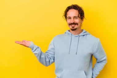 Sarı arka planda izole edilmiş genç beyaz bir adam bir palmiye üzerinde fotokopi alanı gösteriyor ve belinde başka bir el tutuyor..