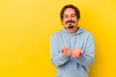 Sarı arka planda izole edilmiş genç, beyaz bir adam. Dudaklarını kıvırıyor, avuç içlerini tutuyor ve hava öpücüğü yolluyor..
