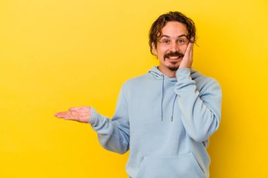 Sarı arka planda izole edilmiş genç beyaz bir adam bir avuç içinde fotokopi alanı tutuyor, el üstünde tutuyor. Şaşırmış ve mutlu..