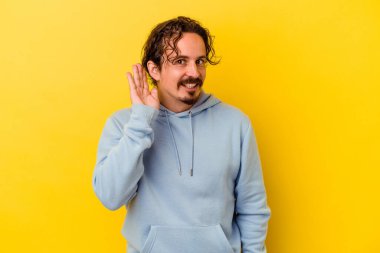 Sarı arka planda izole edilmiş genç beyaz bir adam bir dedikoduyu dinlemeye çalışıyor..