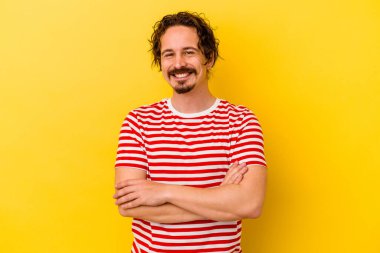 Sarı arka planda izole edilmiş genç beyaz adam kendini güvende hissediyor, kararlılıkla kollarını kavuşturuyor..