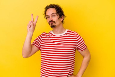 Sarı arka planda izole edilmiş genç beyaz adam neşeli ve kaygısız parmakları olan bir barış sembolü gösteriyor..