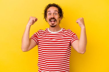 Sarı arka planda izole edilmiş genç beyaz adam tasasız ve heyecanlı bir şekilde tezahürat yapıyor. Zafer konsepti.