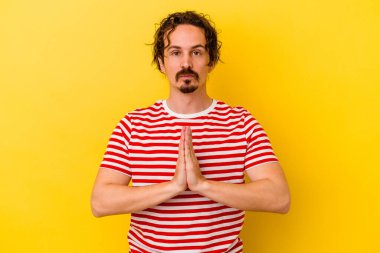 Kafkasyalı genç adam sarı arka planda izole edilmiş dua ediyor, bağlılık gösteriyor, dindar biri ilahi ilham arıyor..