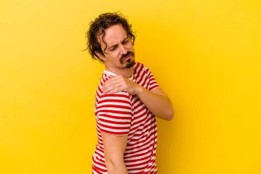 Sarı arka planda izole edilmiş, omuz ağrısı olan genç beyaz bir adam..