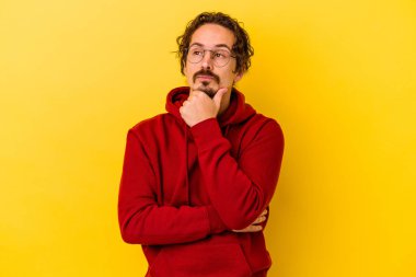 Kafkasyalı genç adam sarı arka planda izole edilmiş düşünüyor ve yukarı bakıyor, yansıtıyor, düşünüyor, hayal kuruyor..