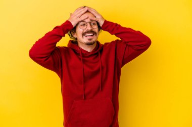 Sarı arka planda izole edilmiş genç beyaz adam ellerini başının üstünde tutarak neşe içinde gülüyor. Mutluluk kavramı.