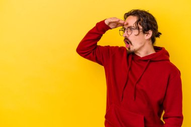 Kafkasyalı genç adam sarı arka planda izole edilmiş, uzaklara bakıyor ve elini alnına koyuyor..