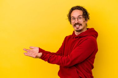 Sarı arka planda izole edilmiş genç beyaz bir adam palmiyesinde bir kopya alanı tutuyor..