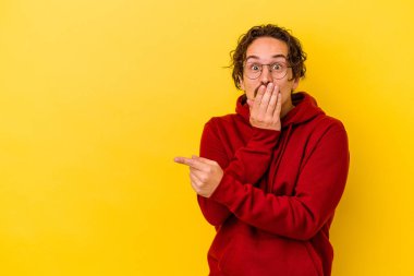 Sarı arka planda izole edilmiş genç beyaz adam yan tarafı işaret ediyor.