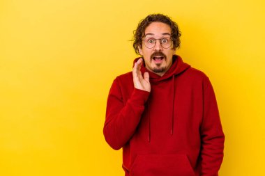 Sarı arka planda izole edilmiş genç beyaz adam yüksek sesle bağırıyor, gözleri açık ve elleri gergin tutuyor..