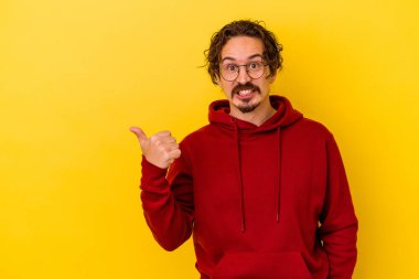 Sarı arka planda izole edilmiş genç beyaz adam işaret parmağıyla fotokopi alanını işaret ederek şok oldu..