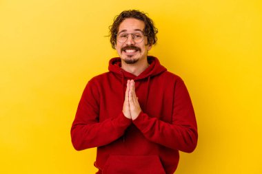 Sarı arka planda izole edilmiş genç beyaz bir adam el ele tutuşup ağız kenarında dua ediyor, kendinden emin hissediyor..