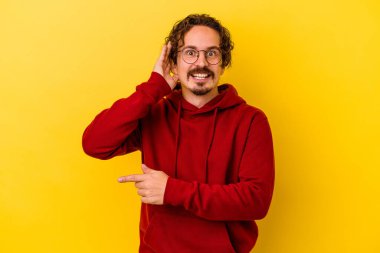 Sarı arka planda izole edilmiş genç beyaz bir adam bir dedikoduyu dinlemeye çalışıyor..