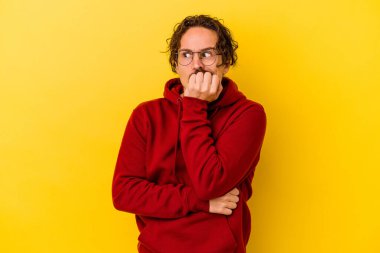 Sarı arka planda izole edilmiş, tırnak yiyen, gergin ve endişeli genç bir beyaz adam..