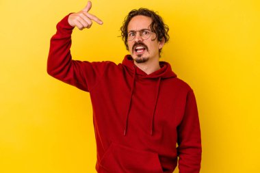 Sarı arka planda izole edilmiş genç beyaz bir adam gömlek fotokopi alanını elle gösteriyor, gururlu ve kendinden emin.