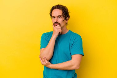 Genç beyaz adam sarı arka planda izole edilmiş şüpheli, belirsiz, seni muayene ediyor..