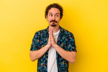Kafkasyalı genç adam sarı arka planda izole edilmiş dua ediyor, bağlılık gösteriyor, dindar biri ilahi ilham arıyor..