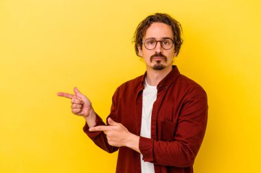 Sarı arka planda izole edilmiş genç beyaz adam işaret parmağıyla fotokopi alanını işaret ederek şok oldu..